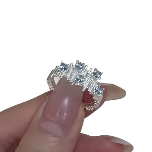 Irregular silver textured ring with five round blue zircons held by fingers