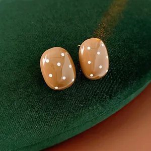 Minimalist oval polka dot earrings in caramel brown finish on dark green velvet