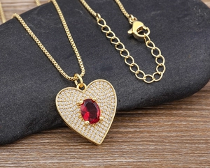 Detailed close-up of golden heart pendant with red stone and pavé zircons on stone background