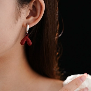 Close-up of model wearing silver heart drop earrings with vintage red enamel finish