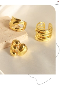 Detail of three-piece golden geometric rings on textured stone and silk background