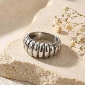 Macro detail of silver stainless steel croissant ring on a warm beige stone surface