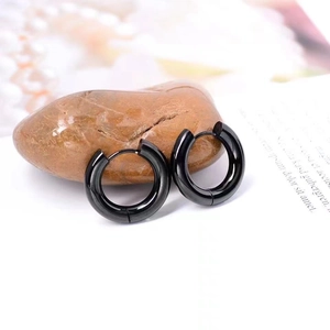 Macro shot of polished black stainless steel hoop earrings on natural pebbles