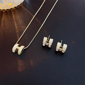 Detailed macro view of gold-plated H-shaped jewelry set with white enamel and zircons