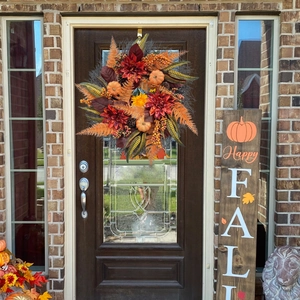 Couronne d'automne avec citrouilles et dahlias sur une porte d'entrée marron foncé