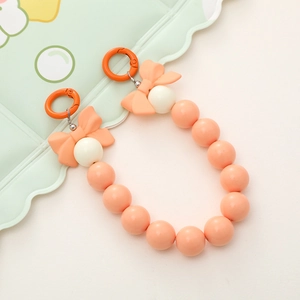 Close-up of orange and cream beaded phone charm with two pink bows on a green tray