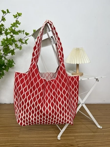 Knitted tote bag with red and white waves hanging on a chair in a cozy home setting