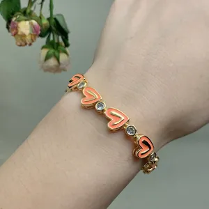 Detail of gold chain bracelet with coral enamel hearts and sparkling zircon stones on wrist
