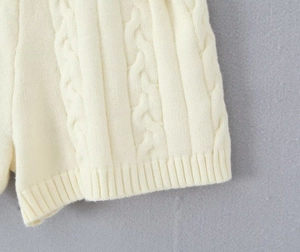 Gros plan détaillé du pull en maille crème avec motifs de torsades et texture côtelée