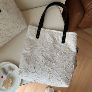 Detail of white quilted tote bag with leaf pattern embroidery and black leather straps