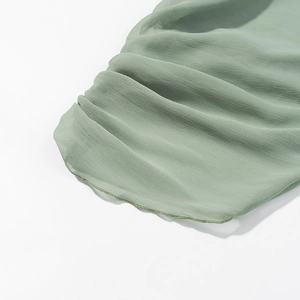 Detailed close-up of light green chiffon fabric with fine pleated hem and precise stitching