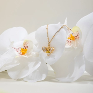 Goldene Bienen-Halskette mit Kristallen und Emaille auf weißer Orchidee