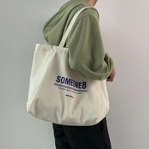 Side view of a large cream canvas tote bag with blue artistic lettering on a model