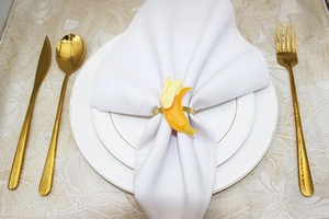 Banana shaped napkin ring in yellow resin on a white plate with golden flatware