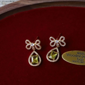 Detailed macro of gold bow teardrop earrings with yellow stones on red velvet background