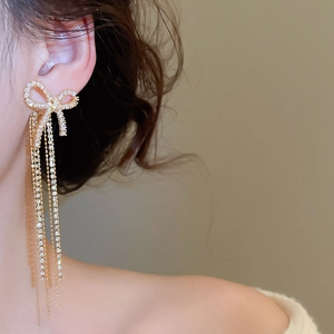 Close-up of elegant bow earrings with sparkling long tassels and gold-plated finish