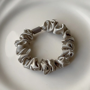 Detailed close-up of a champagne silk scrunchie with a grey matte tube on ceramic