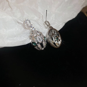 Detailed view of silver oval hoop earrings with white crystals and green gemstones