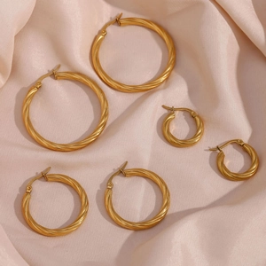 Detailed view of three sizes of gold twisted hoop earrings on champagne silk fabric