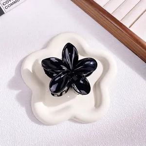 Detail of a glossy black 5-petal flower hair claw clip on a white decorative tray