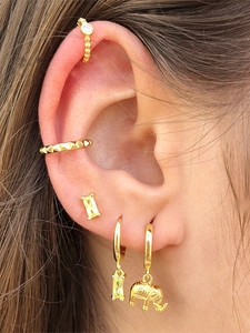 Detail of gold elephant earrings and yellow gemstone studs worn on ear with hair background