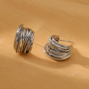 Close-up of silver geometric twisted hoop earrings on orange silk fabric background