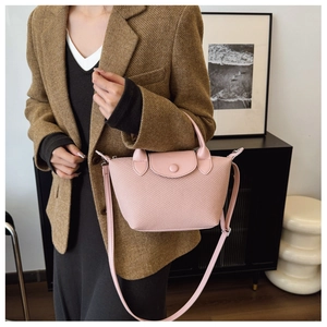 Detail of pink woven texture crossbody bag featuring a curved flap and button closure