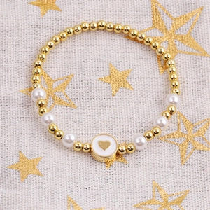 Detail of beaded bracelet with gold beads, white pearls, and heart charm on starry fabric