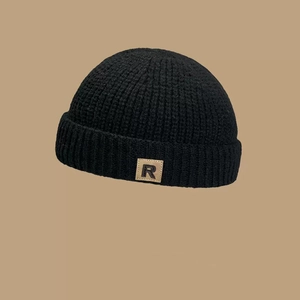 Detalle de gorro de punto negro con parche de cuero caqui y el logo de la letra R