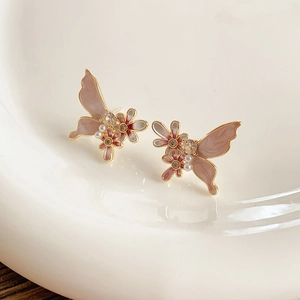 Macro des boucles d'oreilles papillon et fleur dorées avec émail, perles et cristaux