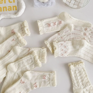 Detail of white ruffle socks featuring pink bows, heart patterns, and textured knit lace