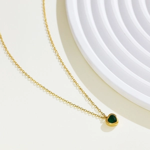 Detail shot of heart necklace with green gemstone and gold chain on white background