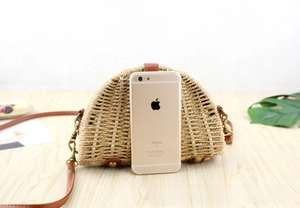 Mini semicircular straw crossbody bag shown next to a smartphone for scale comparison