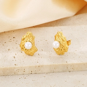Close-up of irregular textured gold earrings with white pearl on beige stone