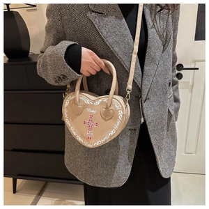 Dettaglio borsa beige a forma di cuore con stampa Baby e croce in un contesto studio
