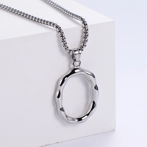 Détail du pendentif anneau ondulé argenté sur une chaîne à billes sur fond blanc