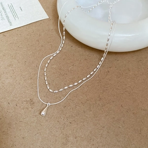 Close-up of double-layer silver necklace featuring a polished water drop pendant