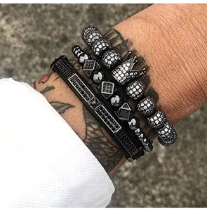 Close-up of black beaded bracelets and crown charm on a male wrist with tattoos