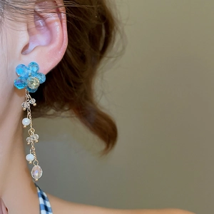Close-up of long tassel earrings with blue crystal flowers and white pearls on a model