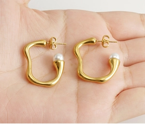 Boucles d'oreilles vagues dorées avec perles blanches présentées sur une main