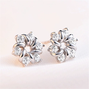 Macro shot of silver flower stud earrings with sparkling white zircons on soft silk