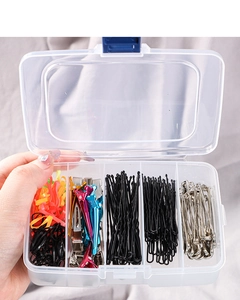 Hand hält eine 5-Fächer-Box gefüllt mit bunten Haarspangen und elastischen Haargummis