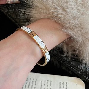 Gros plan d'un bracelet vintage doré avec émail blanc et pierres roses sur un poignet