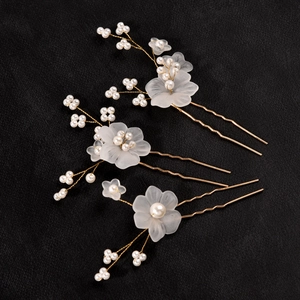 Three elegant white floral bridal hair pins with pearls on a textured black background