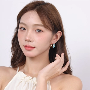 Detailed view of a gold C-shaped earring with a blue turquoise stone worn by a model