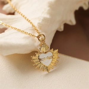 Golden necklace with a white sacred heart pendant on a decorative shell background