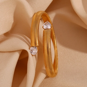 Macro shot of gold-plated twisted bangle with heart-shaped zircon stones on silk