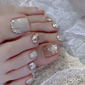Close-up of nude and gold glitter press-on toe nails with rhinestones on white lace