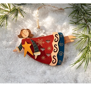 Close-up of painted wooden Christmas angel ornament on snow with pine branch detail