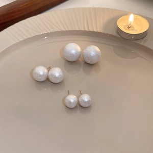 Three pairs of elegant white matte pearl stud earrings on a beige ceramic tray